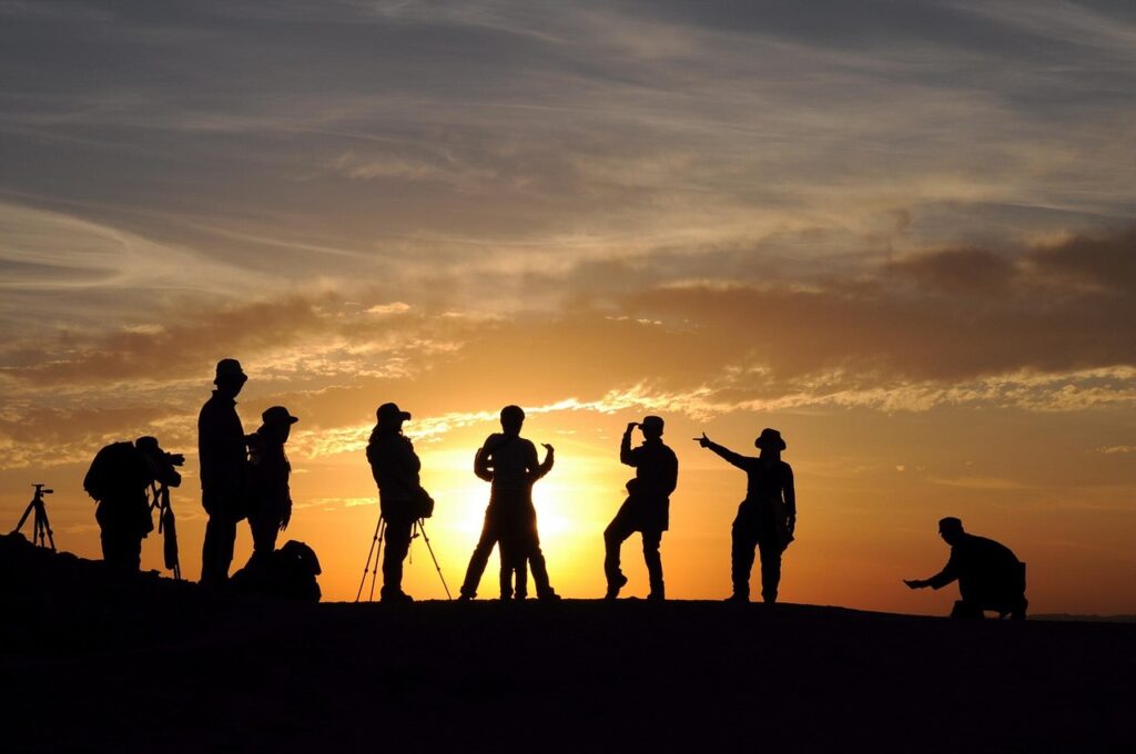 Siluetas de un grupo de fotógrafos y viajeros parados sobre una colina durante un amanecer o atardecer dorado, con cámaras y trípodes apuntando hacia el horizonte en Xinjiang